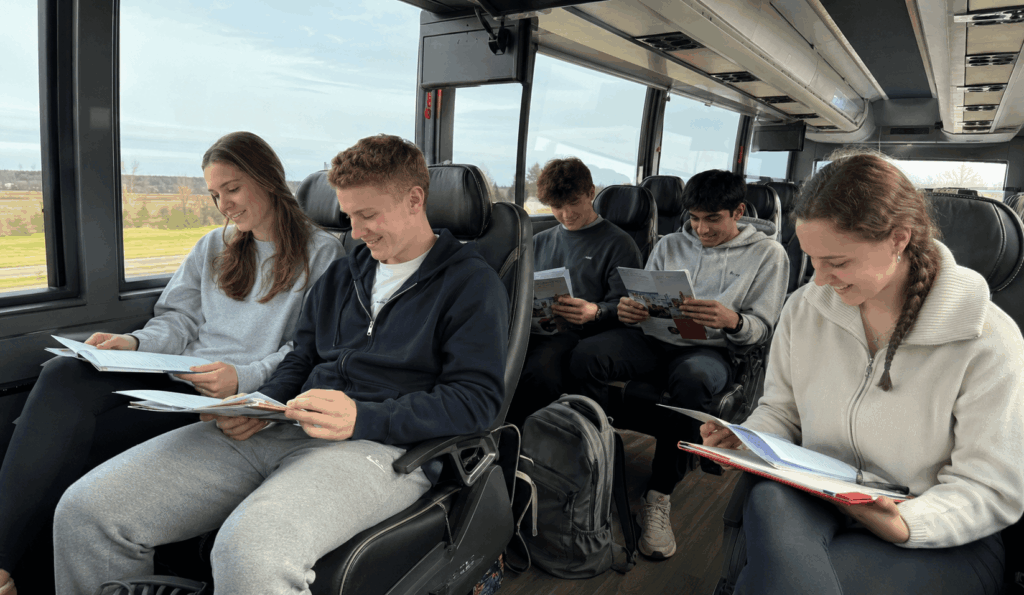 students reviewing college visit materials aboard a charter bus between Indiana campuses